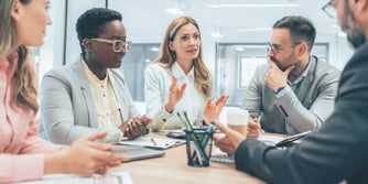 A group of coworkers sit around a conference table talking.