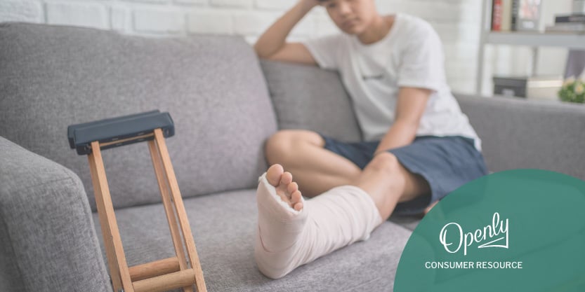 A man with a cast on his leg sits on a couch with crutches. 