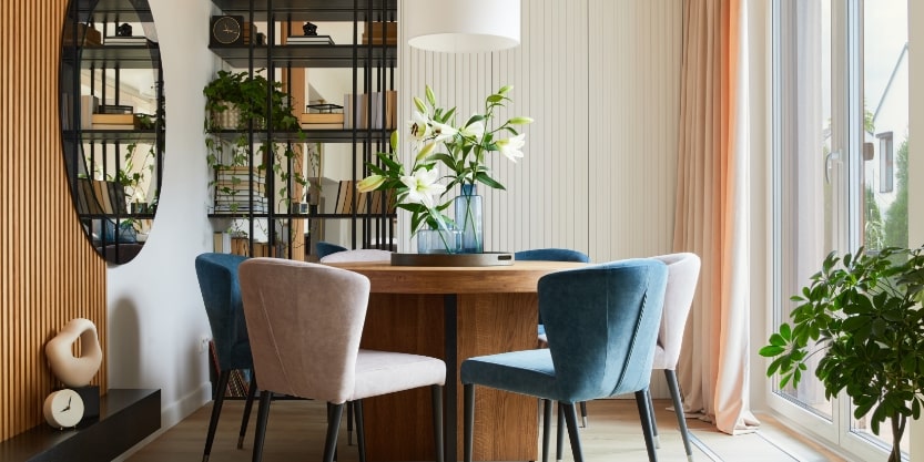 A round table with 3 blue and 3 cream chairs sit around it next to a sliding glass door.