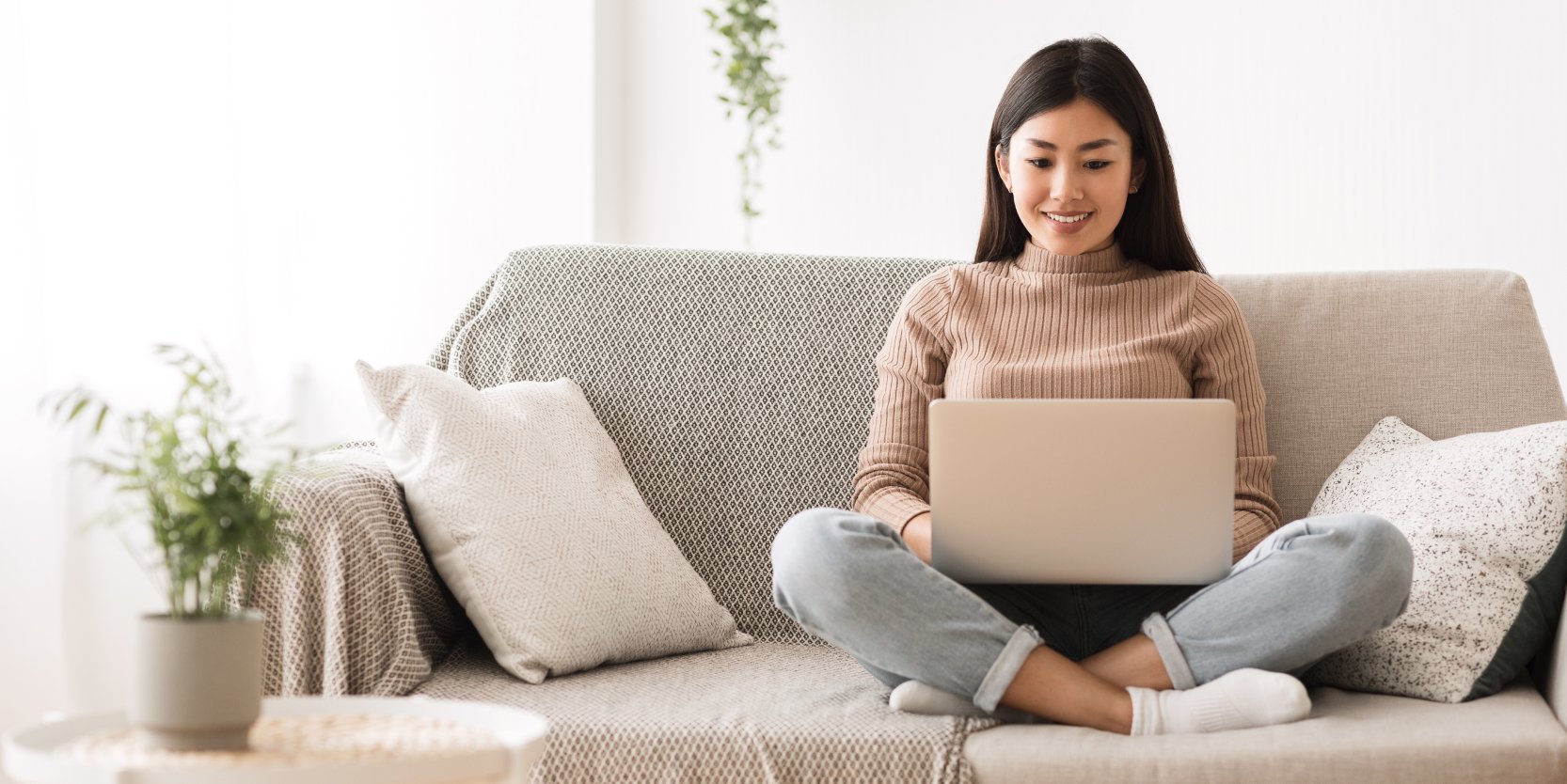  A woman sits on a couch with a laptop in her lap. 
