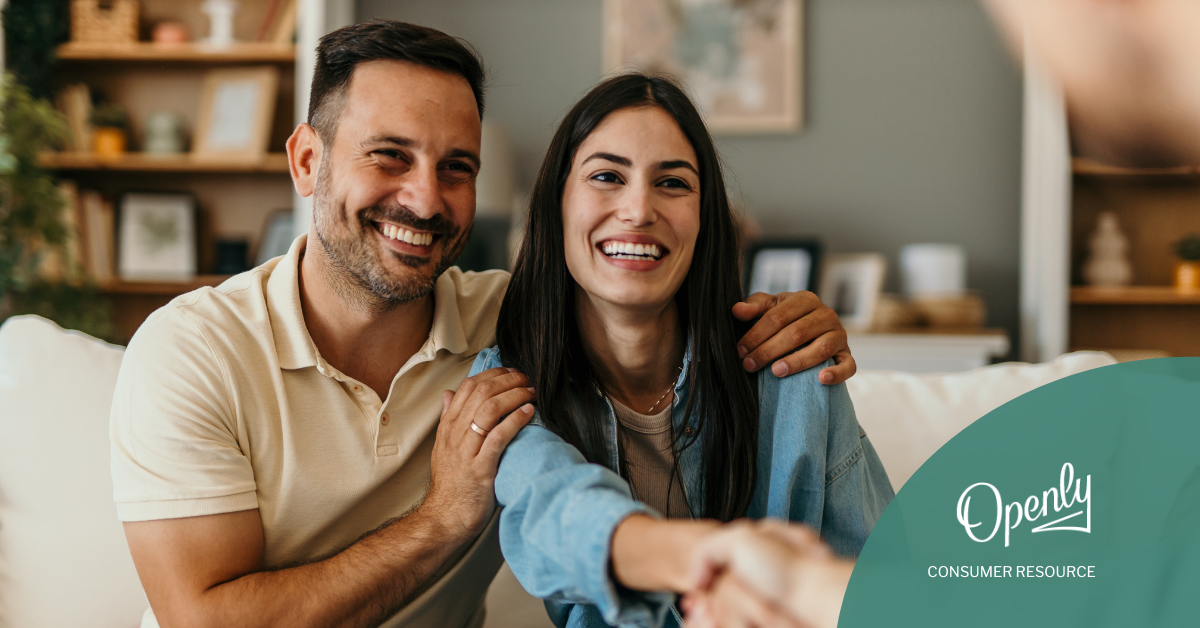 A smiling couple shakes hands with another person. 
