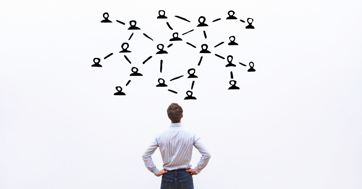 A man looks at a chart of interconnected graphic representations of people on a white board. 